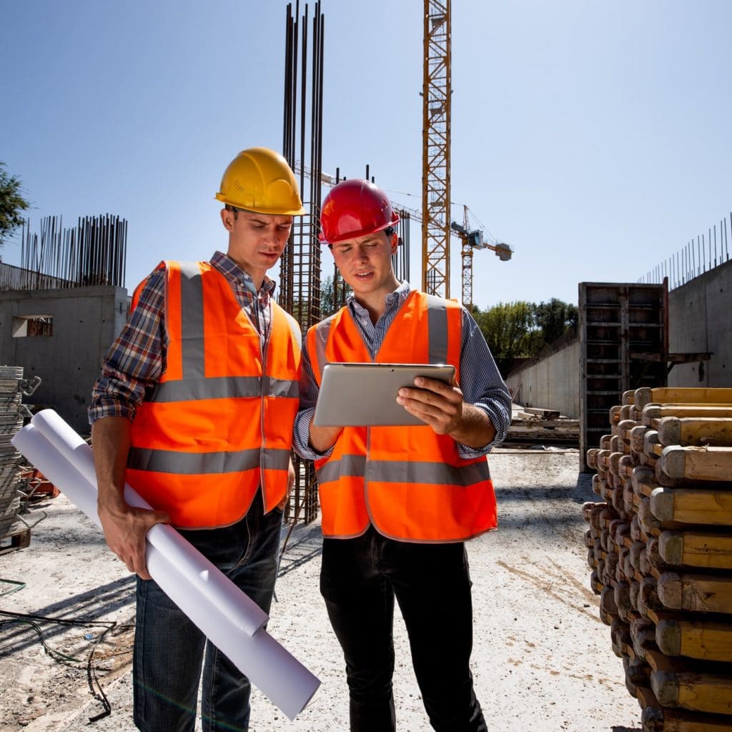 Civil architect and construction manager dressed in orange work vests and helmets discuss a building