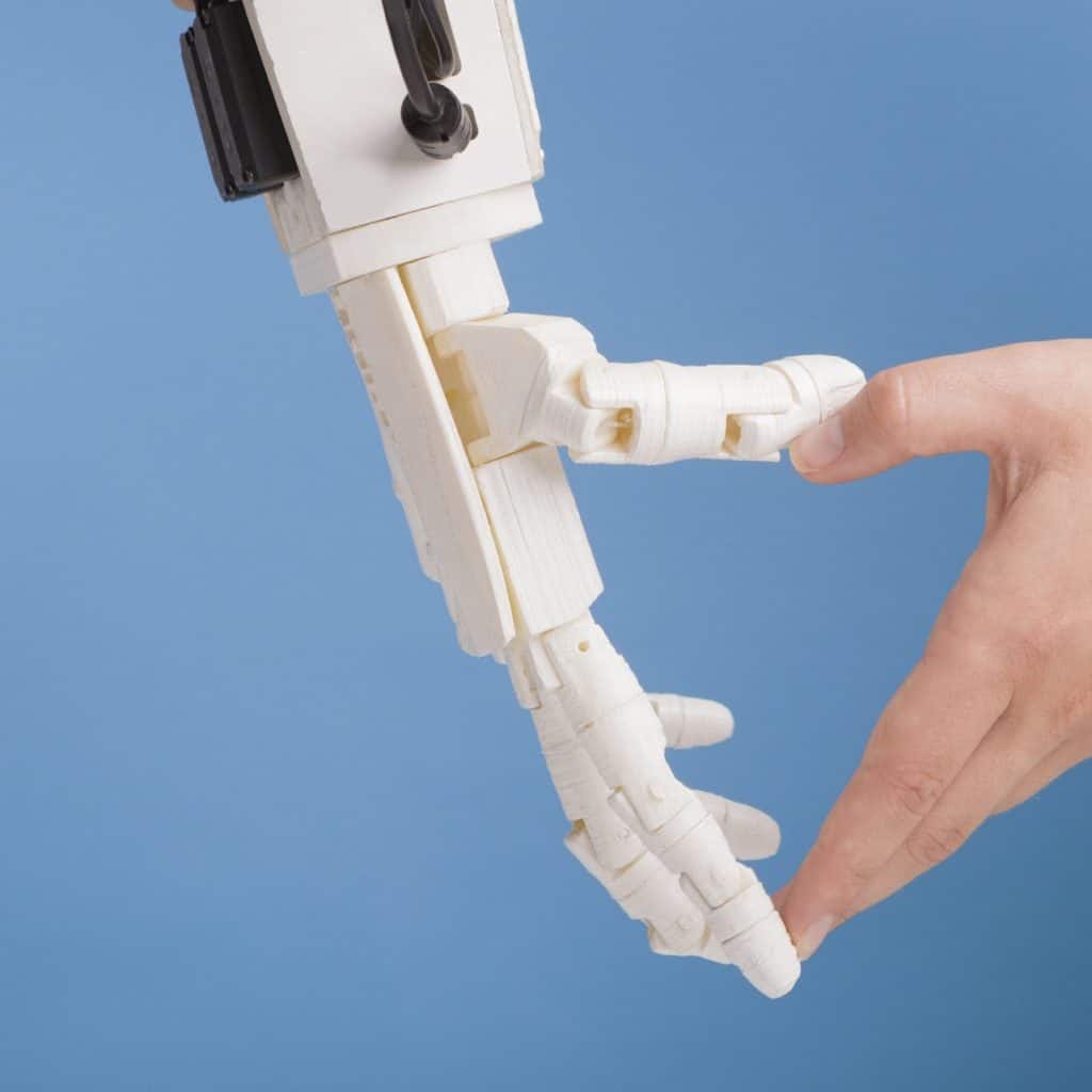Human and robot hands making heart gesture on blue background
