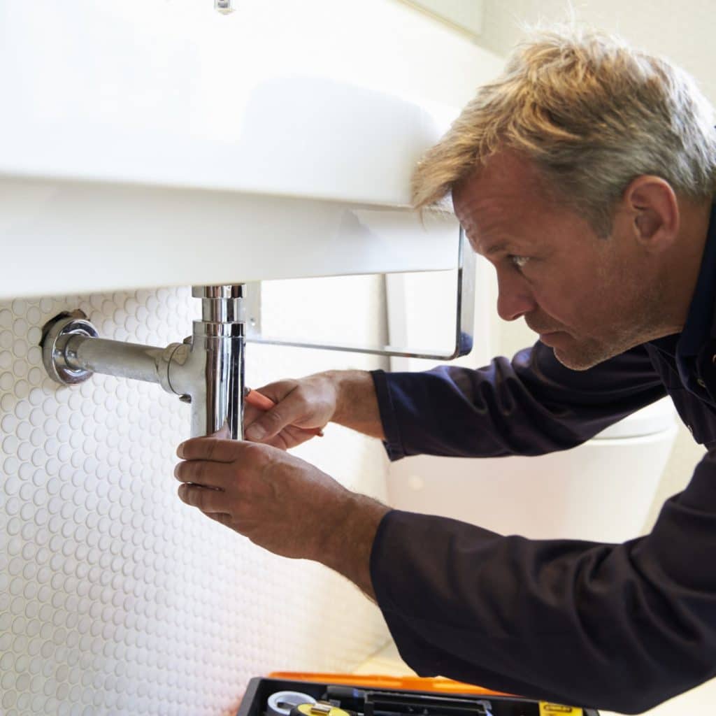 Plumber Working On Sink In Bathroom